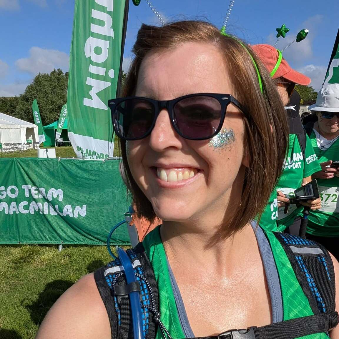 Bright smiling and wearing sunglasses and a green Macmillan vest