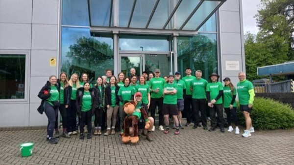 Employees from the Compleat Food group standing outside their office. They're wearing Macmillan T shirts and sport clothes and have a collection bucket.