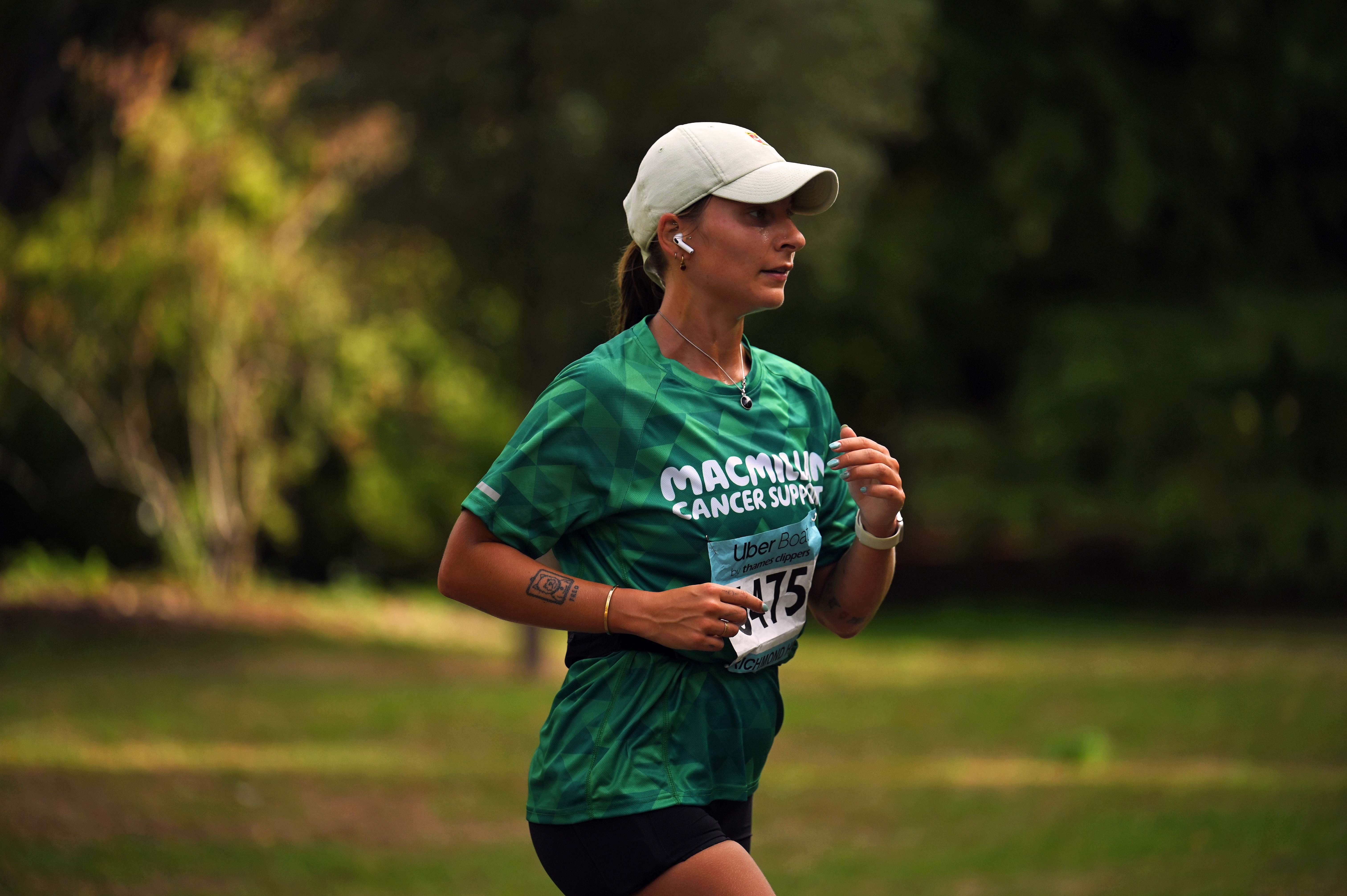 A woman wearing a light cap and Macmillan running t-shirt through a park