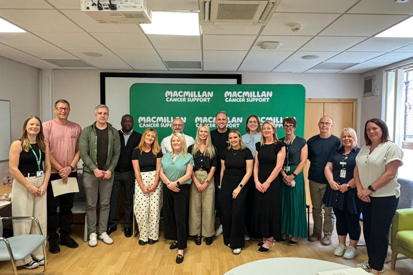 Group of people standing in front of a large green Macmillan Cancer Support board.