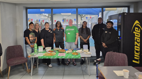 The Balham Leisure Centre hosting a Coffee Morning. They are standing side by side behind a table decorated for the event.