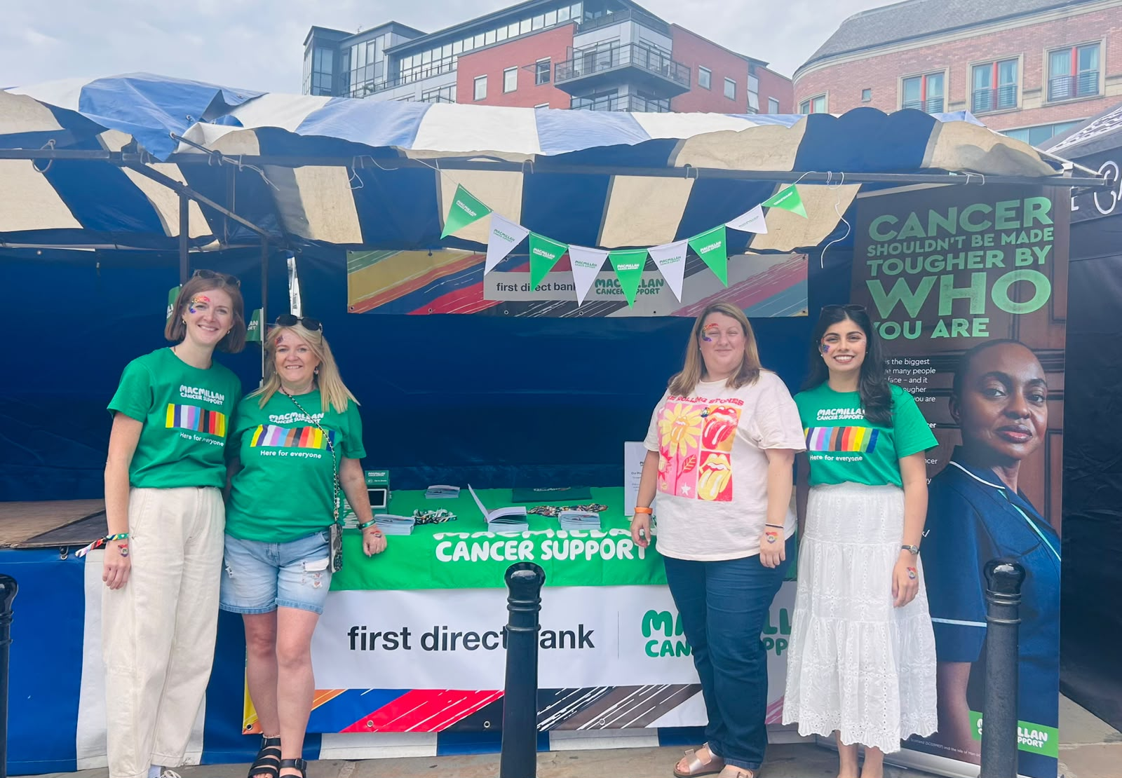 Four people at a Macmillan Cancer Support stand, with Macmillan and first direct branding.