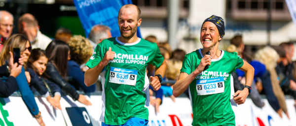 Macmillan runners Marion and Pete running together and smiling while wearing their green Macmillan running t-shirts.