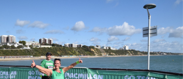 A couple of people running on Bournemouth Pier wearing green Macmillan t-shirts. One of them is giving a double thumbs up to the camera. 