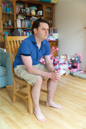Position 2. A man sits on a chair. His feet are flat on the floor. He leans forward, resting his elbows on his thighs. His knees are shoulder width apart.