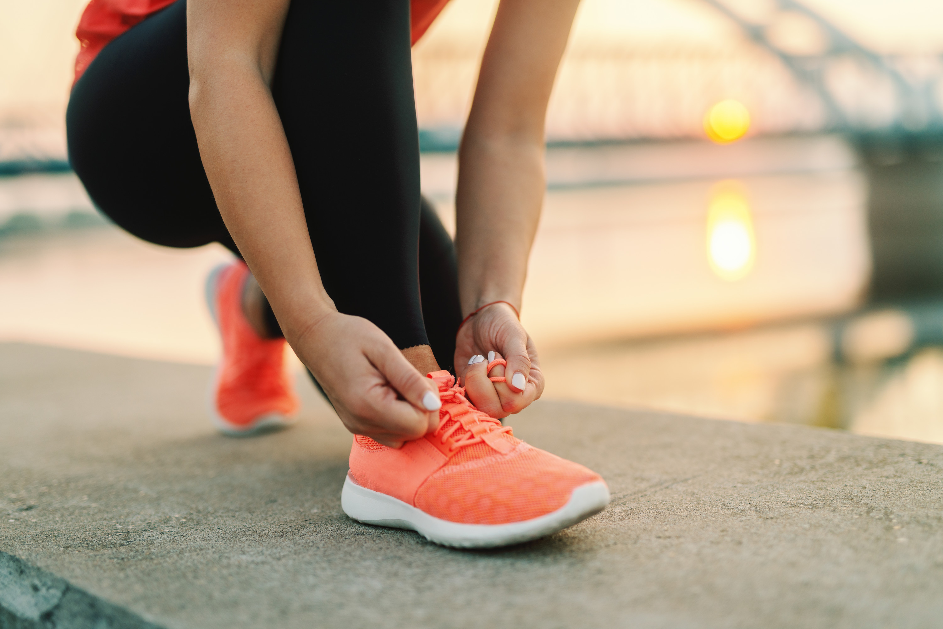 A woman crouching down tying the laces on her bright orange trainers