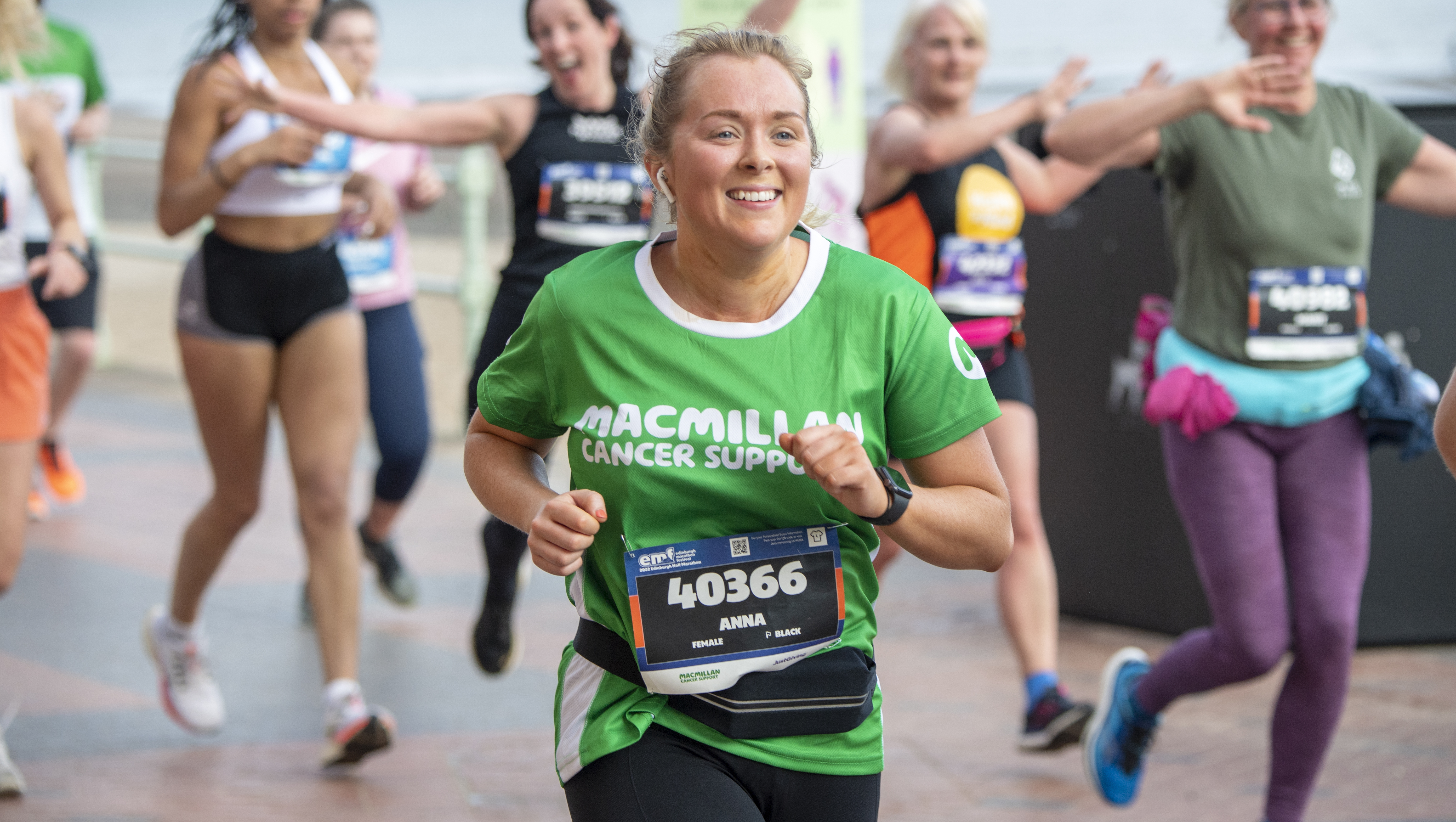Woman running wearing a Macmillan running t-shirt surrounded by other runners