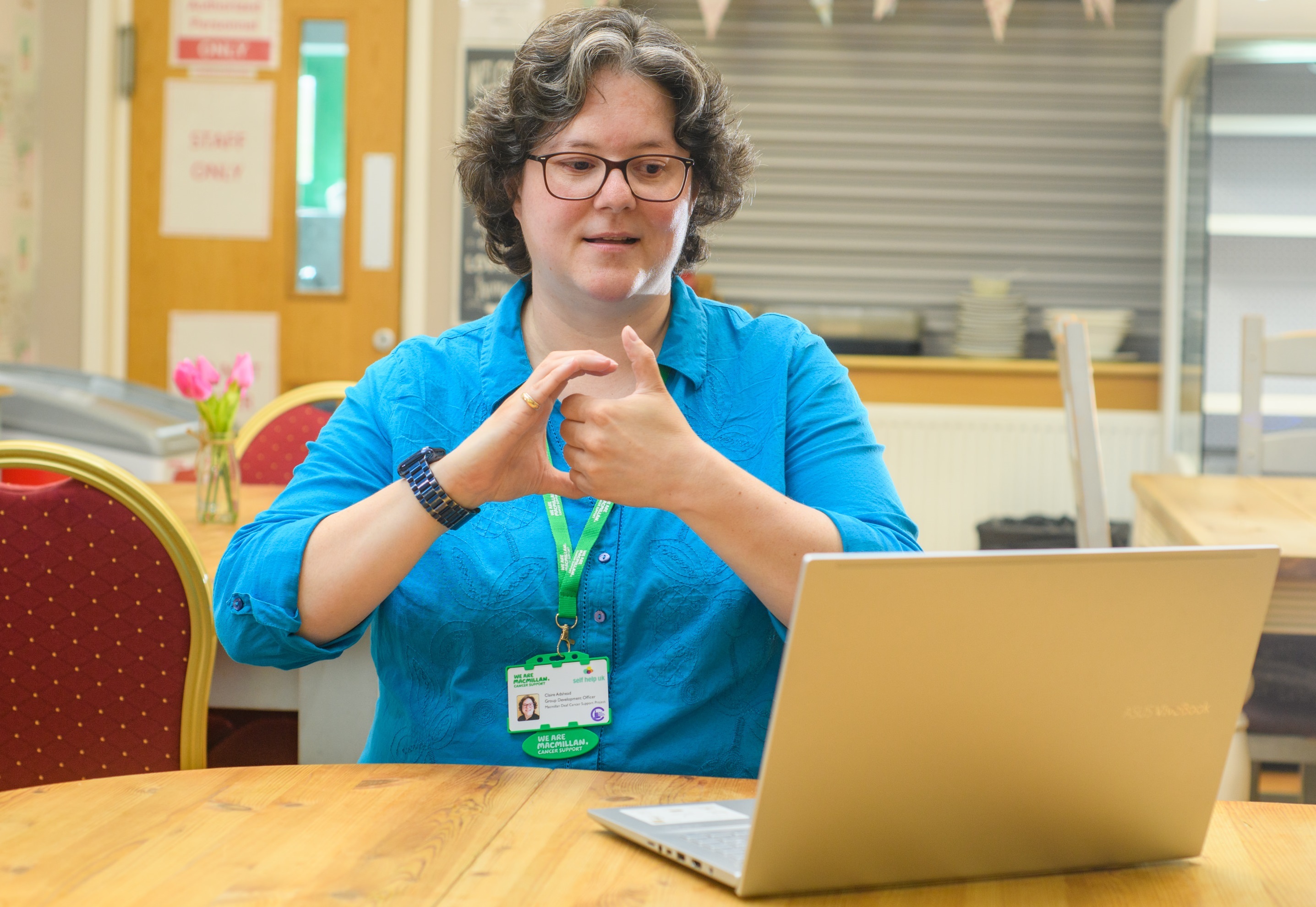 Woman wearing a Macmillan lanyard sits at desk on a video call using BSL