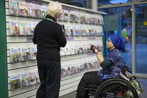 A woman in a wheelchair looking at Macmillan information leaflets and speaking to a Macmillan employee