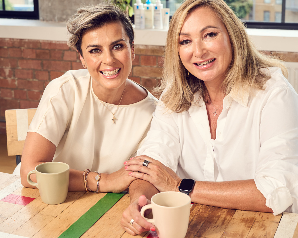Melissa and Marina smiling and sitting at a table with cups of coffee. La Roche Possay products are shown behind them.