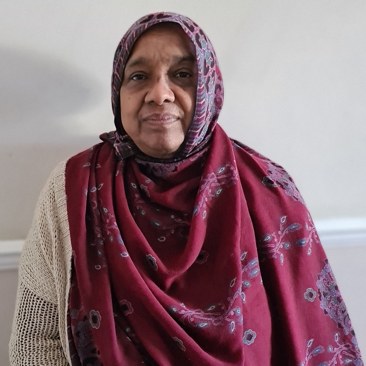 An Asian lady wearing a cream cardigan and a dark red scarf.