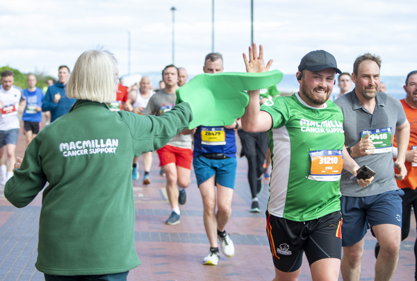 A Macmillan volunteer with a big green foam hand high fiving a Macmillan runner as they run past
